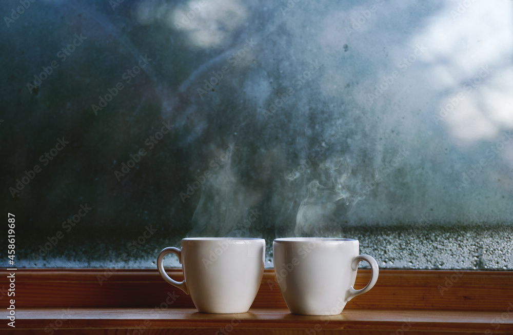 Two cup of hot drink coffee near window, water condensation on window glass, early morning, wake up concept Two cup of hot drink coffee near window, water condensation on window glass, early morning, wake up concept
