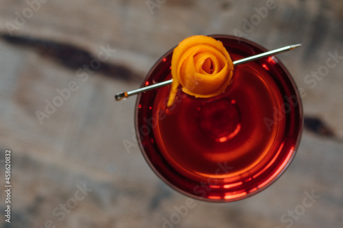 bright red cocktail boulevardier top down shot with orange peel rose garnish on whiskey bourbon barrel 