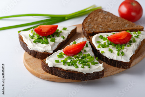 Slices of bread with cottage cheese, onion and tomatoes on wooden plate on white background