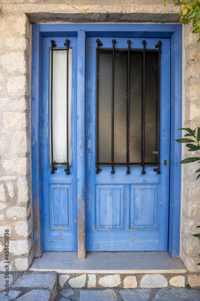 Entrance closed door with blue shutters, glass window and iron-shod details. Greek traditional house with stone walls. Summer travel locations architecture