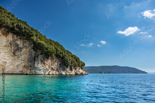 Blue Ormos Desimi clear calm Ionian Sea water with scenic green rocky cliffs coast and bright sky. Nature of Lefkada island in Greece. Summer vacation idyllic travel destination