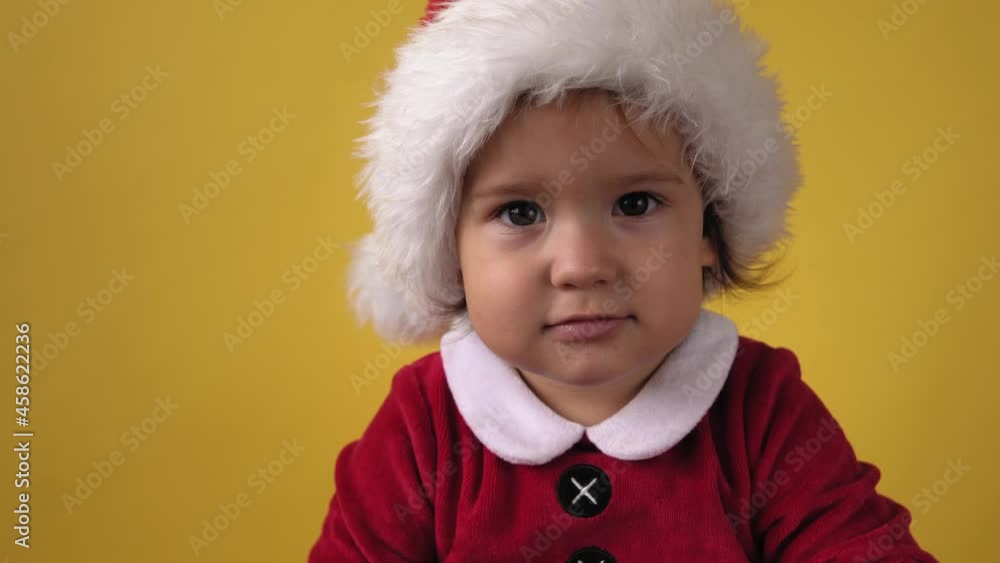 Close up emotion Cute Happy Cheerful Chubby Toddler Baby Girl in Santa Suit Looking On Camera At Yellow Background. Child Playing Christmas Scene Celebrating Birthday. Kid Have Fun Spend New Year Time Close up emotion Cute Happy Cheerful Chubby Toddler Baby Girl in Santa Suit Looking On Camera At Yellow Background. Child Playing Christmas Scene Celebrating Birthday. Kid Have Fun Spend New Year Time