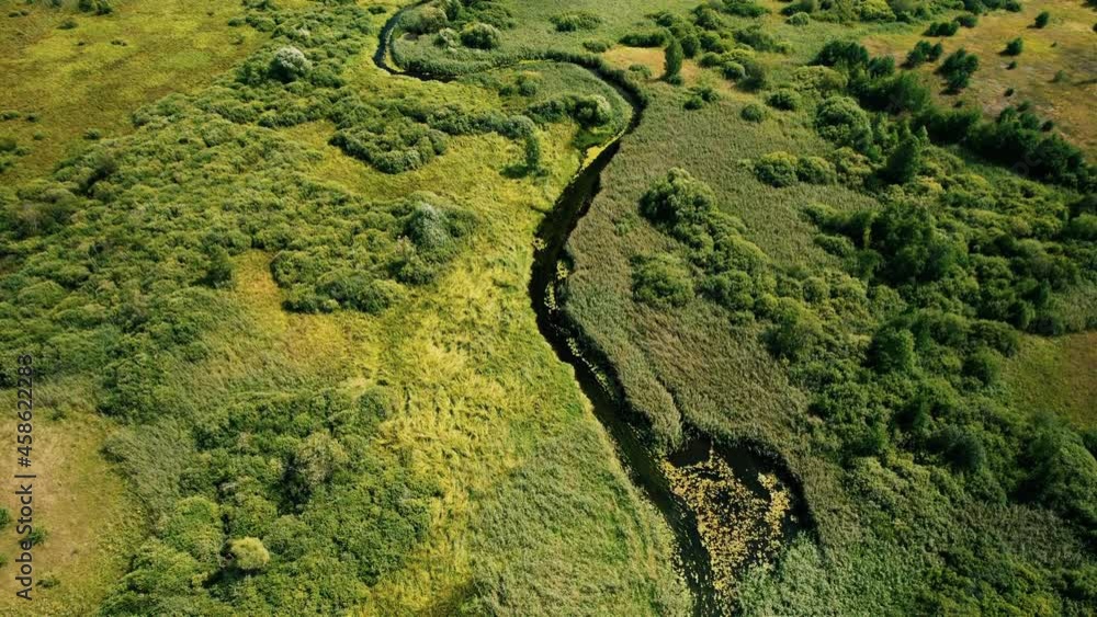 River in the wild. Aerial view of small river in middle of green field and forest in the wilderness. Natural Resource and Ecosystem. Wildlife Refuge Wetland Restoration. European Green Nature Scenery. River in the wild. Aerial view of small river in middle of green field and forest in the wilderness. Natural Resource and Ecosystem. Wildlife Refuge Wetland Restoration. European Green Nature Scenery.