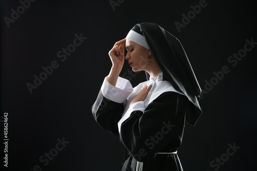Young praying nun on dark b...