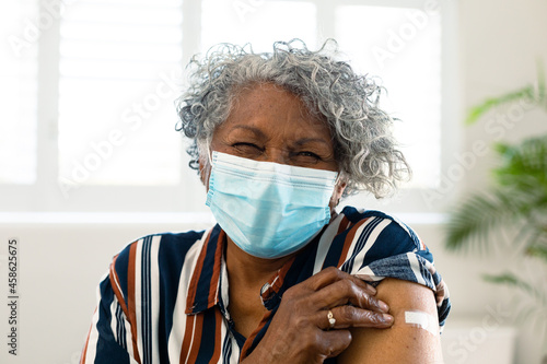 Happy senior african american woman wearing face mask with plaster on arm after vaccination