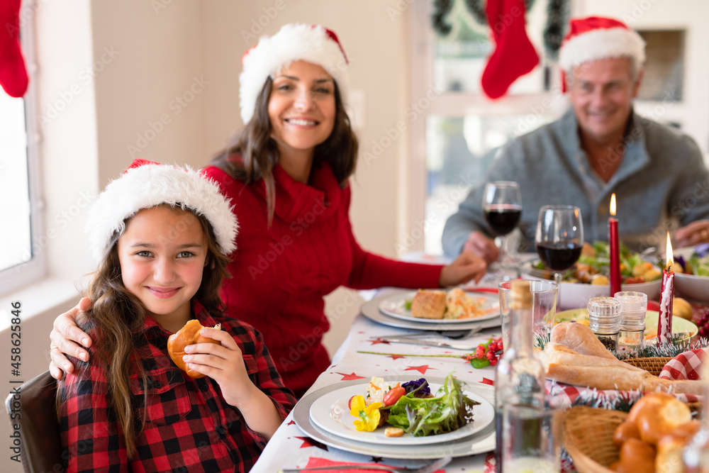 Happy caucasian mother and daughter wearing santa hats looking at camera at christmas time Happy caucasian mother and daughter wearing santa hats looking at camera at christmas time