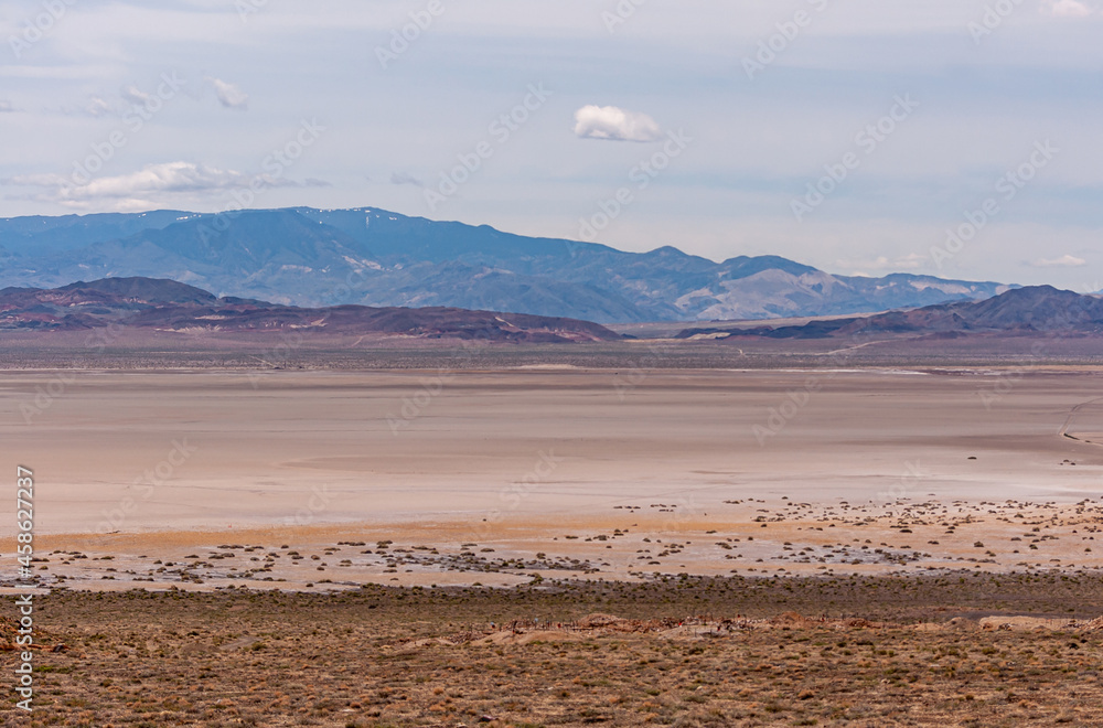 High Desert, Nevada, USA - May 17, 2011: Wide landscape with flat beige colored dry lake with mountain range in back under gray cloudscape..