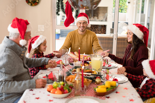 Caucasian multi generation family wearing santa hats praying at christmas table