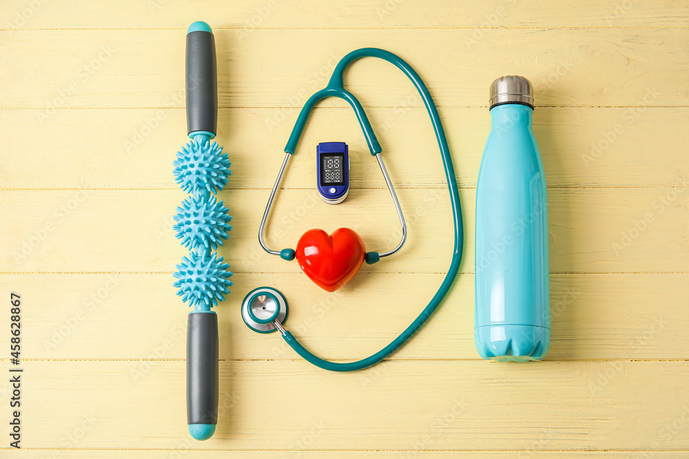 Composition with pulse oximeter, stethoscope, bottle of water, body roller and red heart on color wooden background Composition with pulse oximeter, stethoscope, bottle of water, body roller and red heart on color wooden background