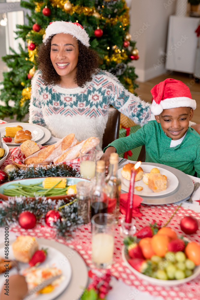 Happy african american mother and son wearing santa hats sitting at christmas table Happy african american mother and son wearing santa hats sitting at christmas table