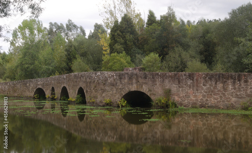 Ponte medieval construída em pedra em espelho na água do rio com árvores e arbustos por trás