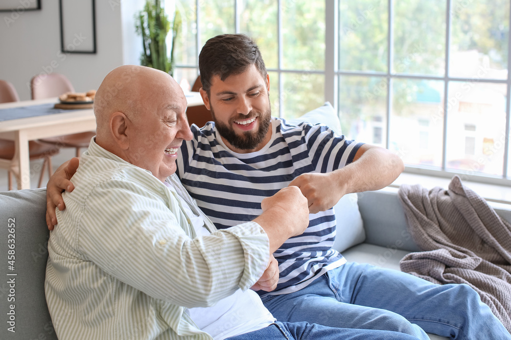 Happy man and his father bumping fists while sitting on sofa at home Happy man and his father bumping fists while sitting on sofa at home