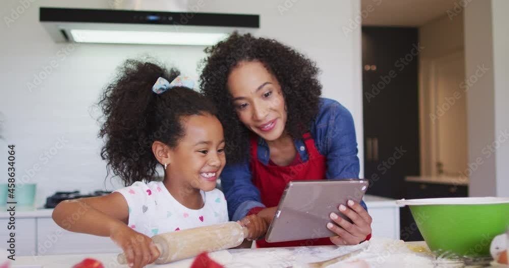 Happy african american mother and daughter using tablet and baking together Happy african american mother and daughter using tablet and baking together