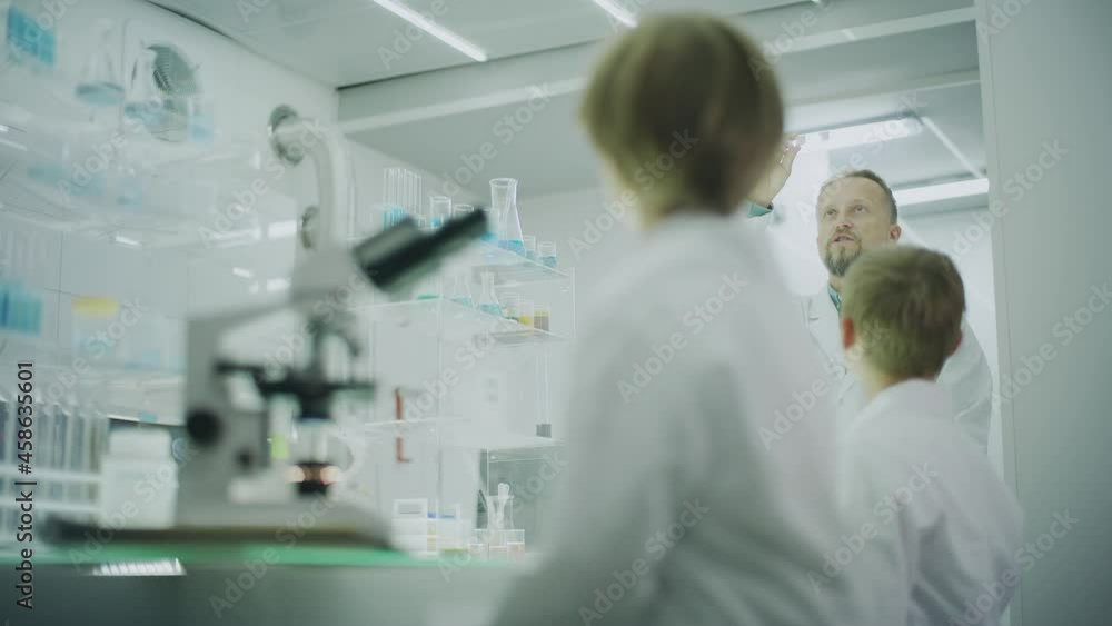 Boy focused on work in laboratory. Using microscope, friend and teacher in background Boy focused on work in laboratory. Using microscope, friend and teacher in background