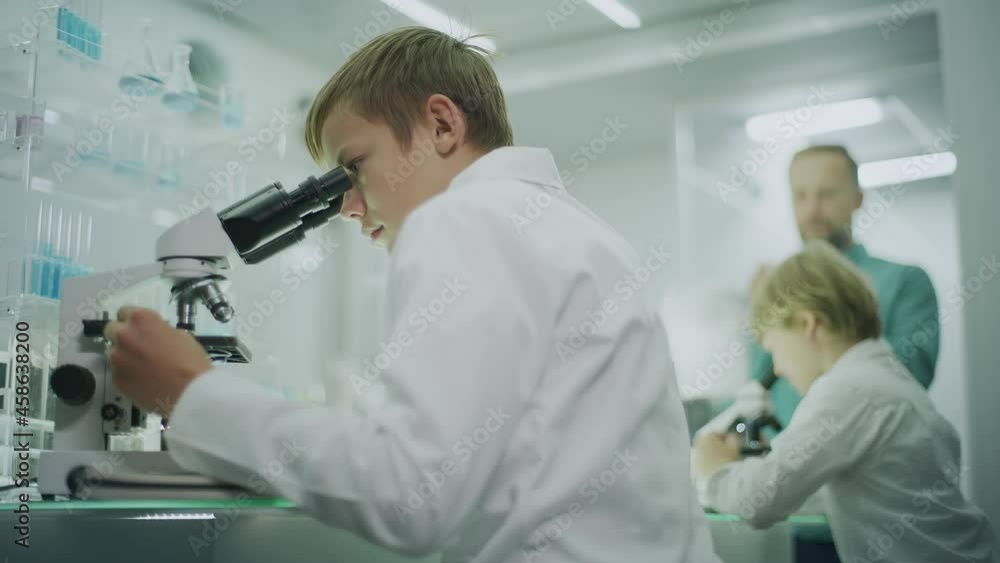 Boy focused on work in laboratory. Using microscope, friend and teacher in background Boy focused on work in laboratory. Using microscope, friend and teacher in background