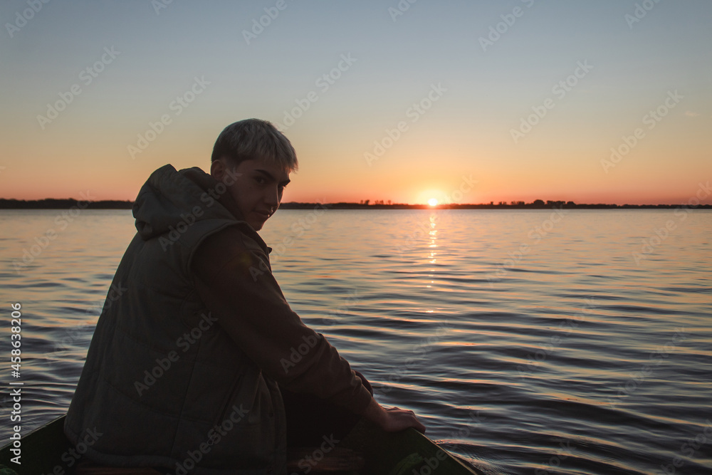 Handsome young man sailing in a small boat on the sea towards sunset.