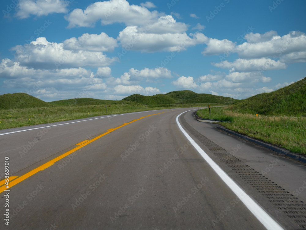 Winding paved road with gently rolling hills and beautiful clouds in the skies, Nebraska, USA.