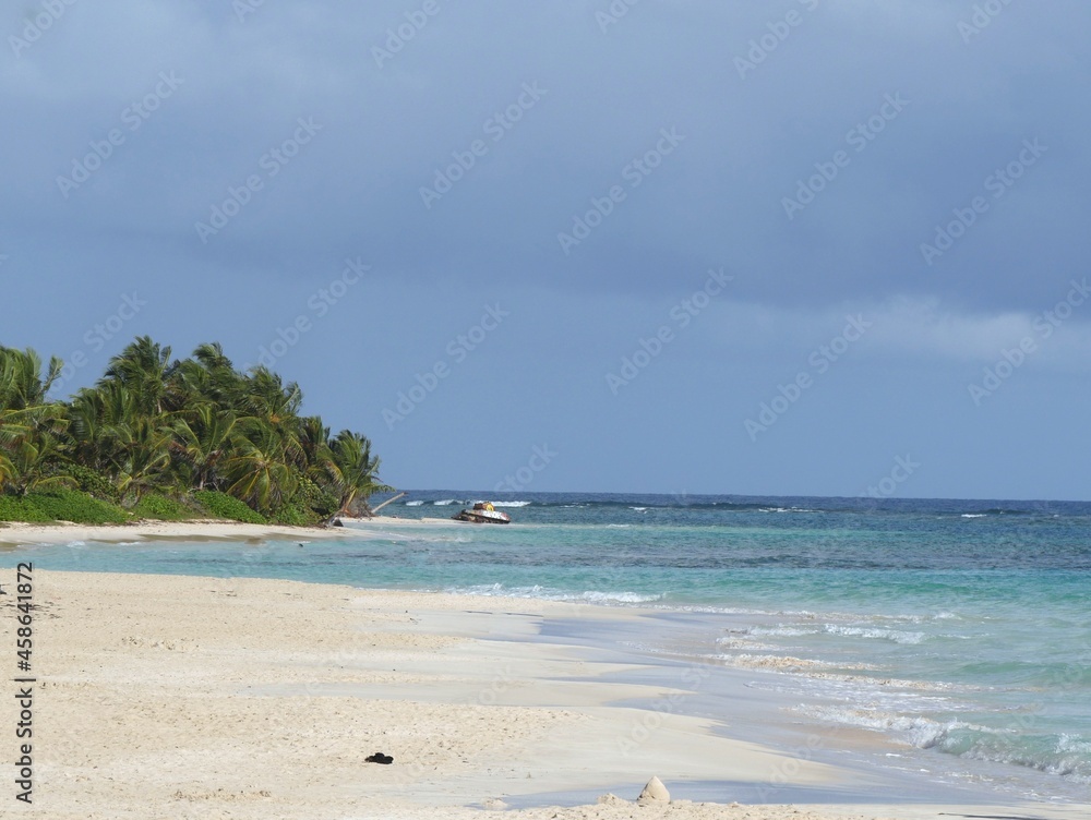 Naklejka premium Waves rolling into a white sand Flamenco beach in Culebra, Puerto Rico, with an old tanker in the distance.