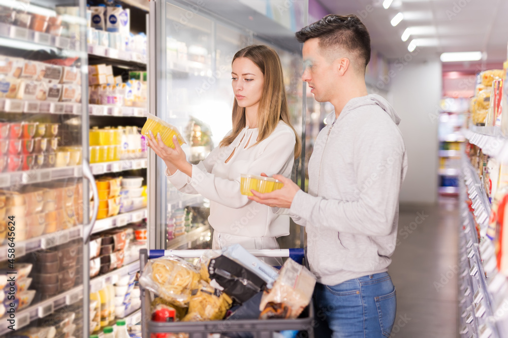 Family shopping, young man and woman choosing yogurt and other dairy products in supermarket.