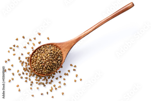 uncooked buckwheat in the wooden spoon, isolated on the white background, top view