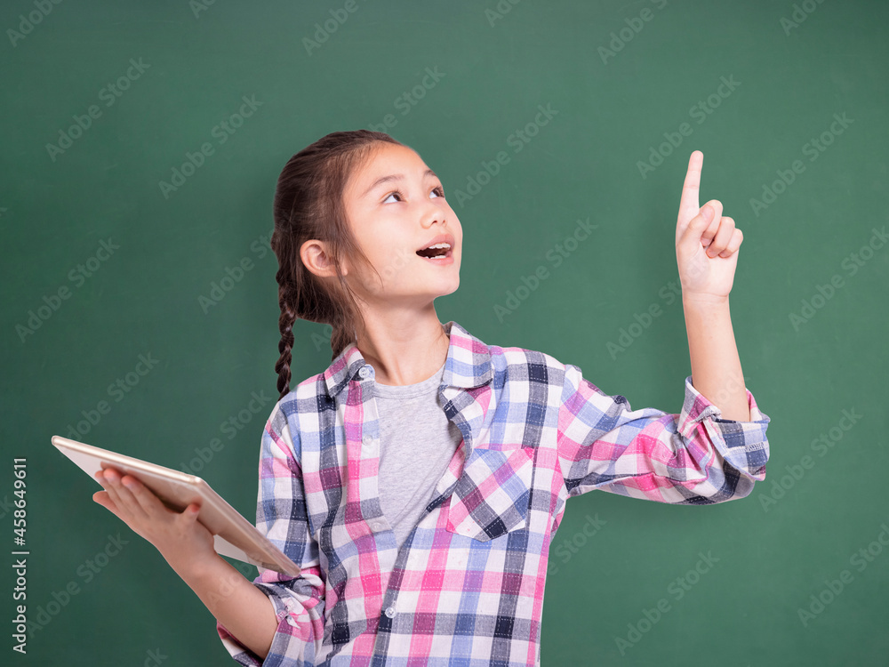 Happy student girl holding tablet and pointing upside.Isolated on green chalkboard background.. Happy student girl holding tablet and pointing upside.Isolated on green chalkboard background..