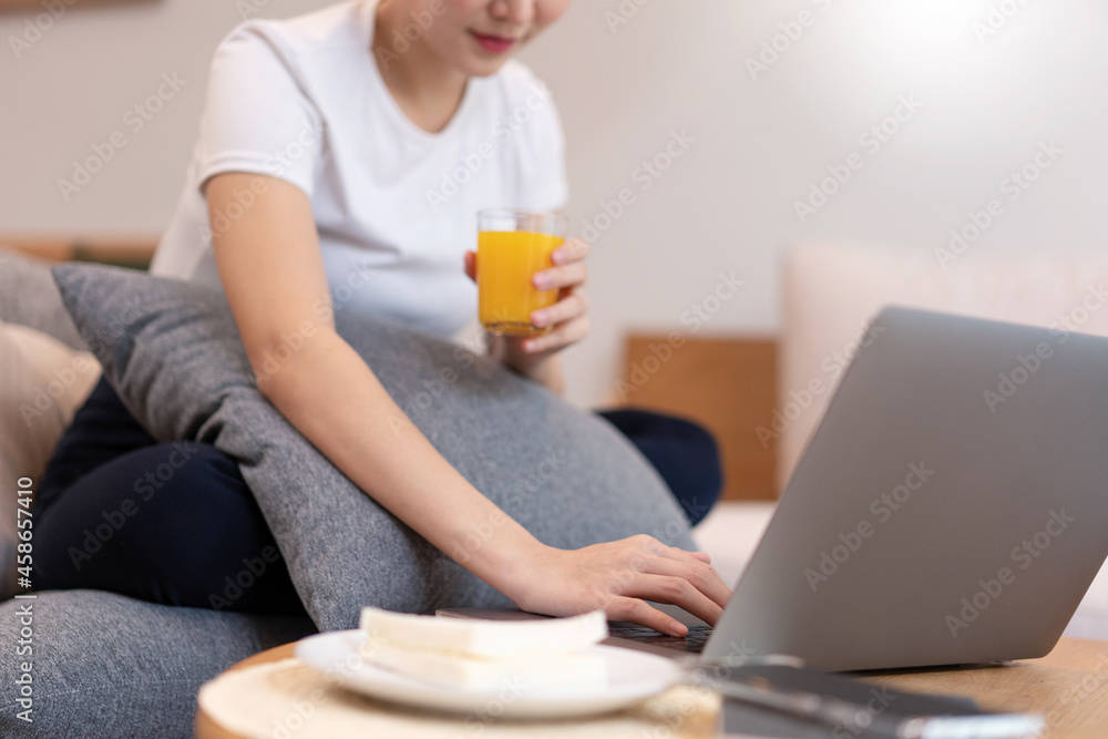 Living room concept in the coffee shop a girl with a bun hair using her laptop going on the internet with a glass of orange juice Living room concept in the coffee shop a girl with a bun hair using her laptop going on the internet with a glass of orange juice