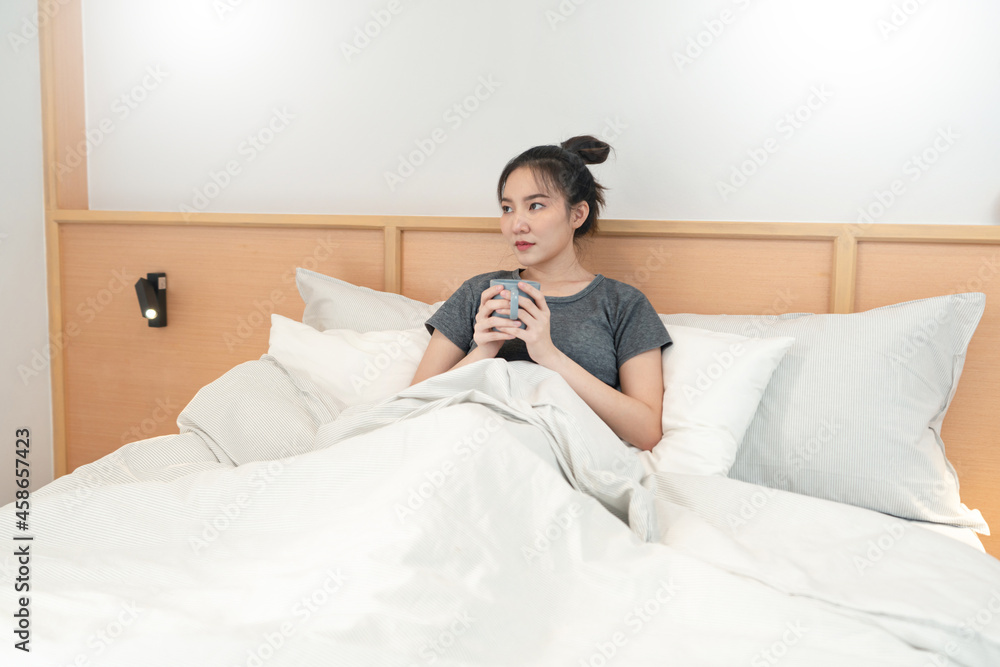 Bedroom concept in the bed a girl appreciating a scent and a taste of the hot coffee in her hands gazing outside the window Bedroom concept in the bed a girl appreciating a scent and a taste of the hot coffee in her hands gazing outside the window