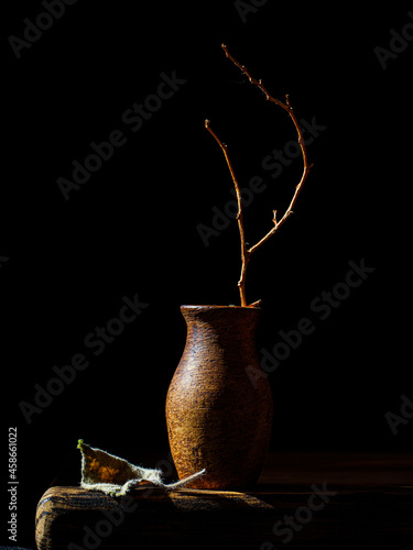 Herfst vernietigende minimalistische Stilleven met verdorde tak in klei vaas en droog blad op houten tafel Verticaal, low key, zijaanzicht. Nederlandse stillevenstijl
