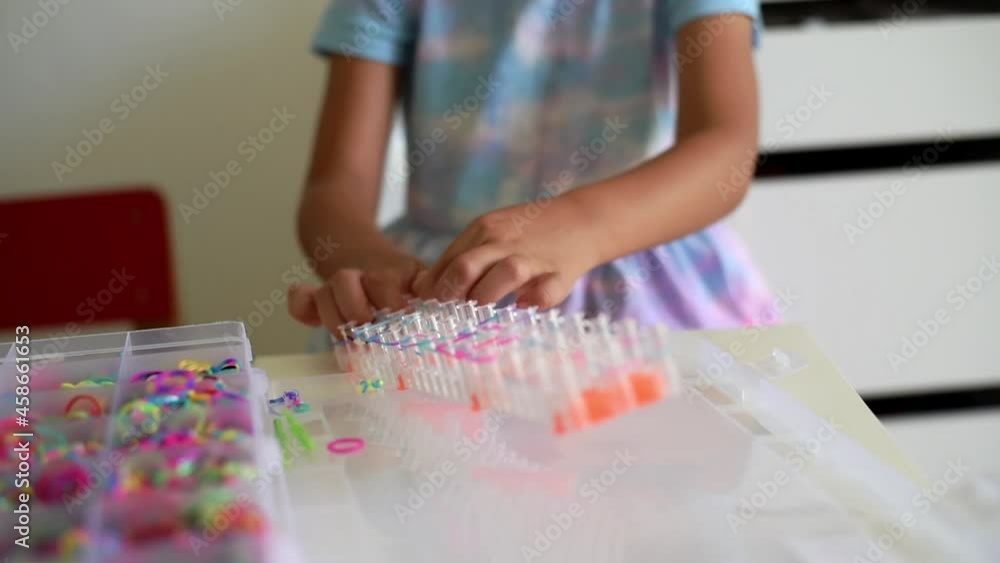 Hands of small girl playing and making accessories bracelet from silicone rubber bands. light background. collect necklace by hook. hobby of small girl. make gift for for friend Hands of small girl playing and making accessories bracelet from silicone rubber bands. light background. collect necklace by hook. hobby of small girl. make gift for for friend