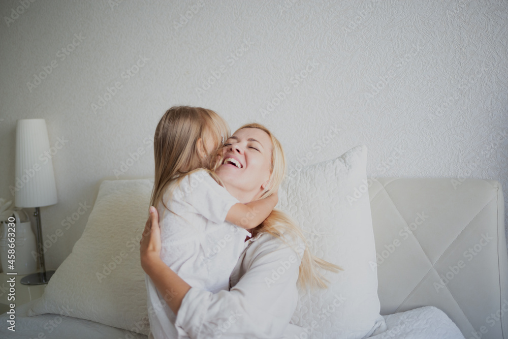 little girl hugging with mom while sitting on the bed in the bedroom little girl hugging with mom while sitting on the bed in the bedroom