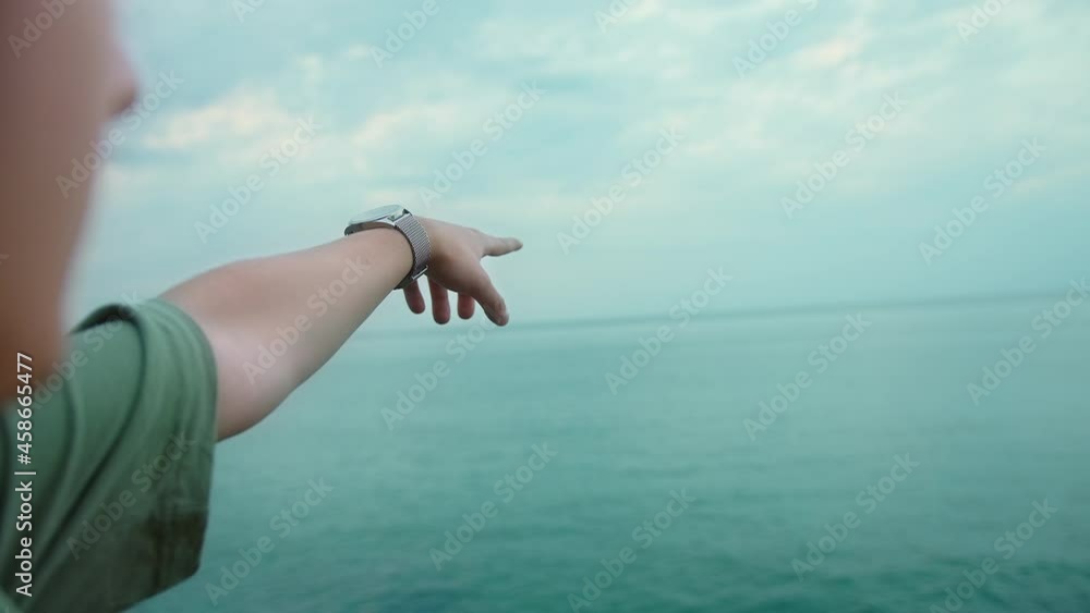 Young man pointing to the horizon with his forefinger while looking out to sea Young man pointing to the horizon with his forefinger while looking out to sea
