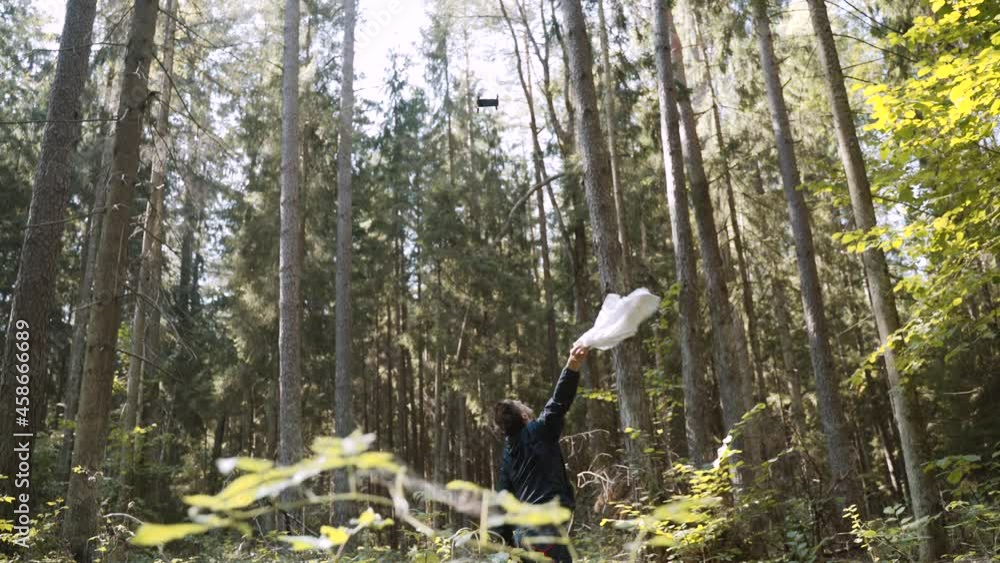 Dark-haired young thin man was lost in forest. Guy waves white rag to get attention, signal sos of rescuers. Drone flies up to the lost person. Cloth flies away, man continues to wave his hand. Dark-haired young thin man was lost in forest. Guy waves white rag to get attention, signal sos of rescuers. Drone flies up to the lost person. Cloth flies away, man continues to wave his hand.