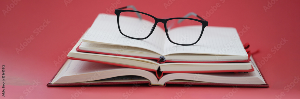 Glasses for sight lying on pile of notebooks on red background closeup