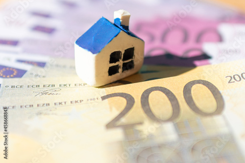 Miniature toy house placed on Euro bill banknotes. Concept for real estate costs, prices, buy or rent a house, hypothecary credit, interest.Selective focus,closeup.Blurred background and foreground. photo