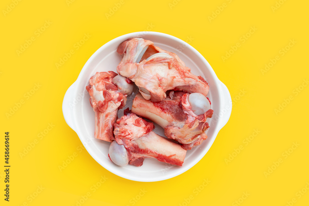 Raw pork bones in white plate on yellow background.