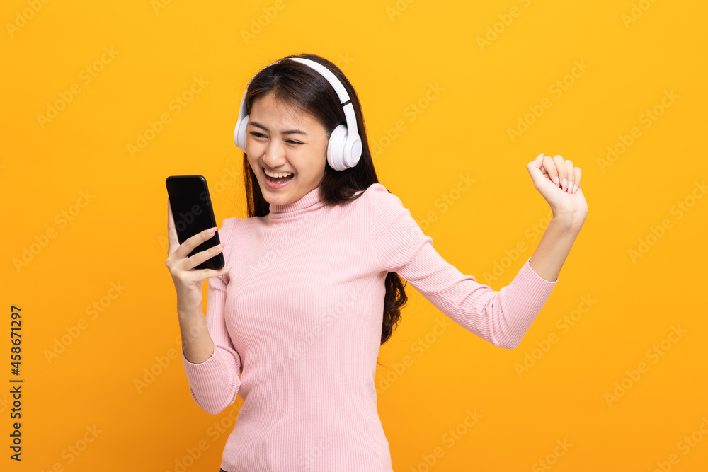 Beautiful young asian women choose song and play music from smartphone connection with wireless headphone having fun. Teenage girl listen to the music enjoy relaxing on isolated yellow background. Beautiful young asian women choose song and play music from smartphone connection with wireless headphone having fun. Teenage girl listen to the music enjoy relaxing on isolated yellow background.