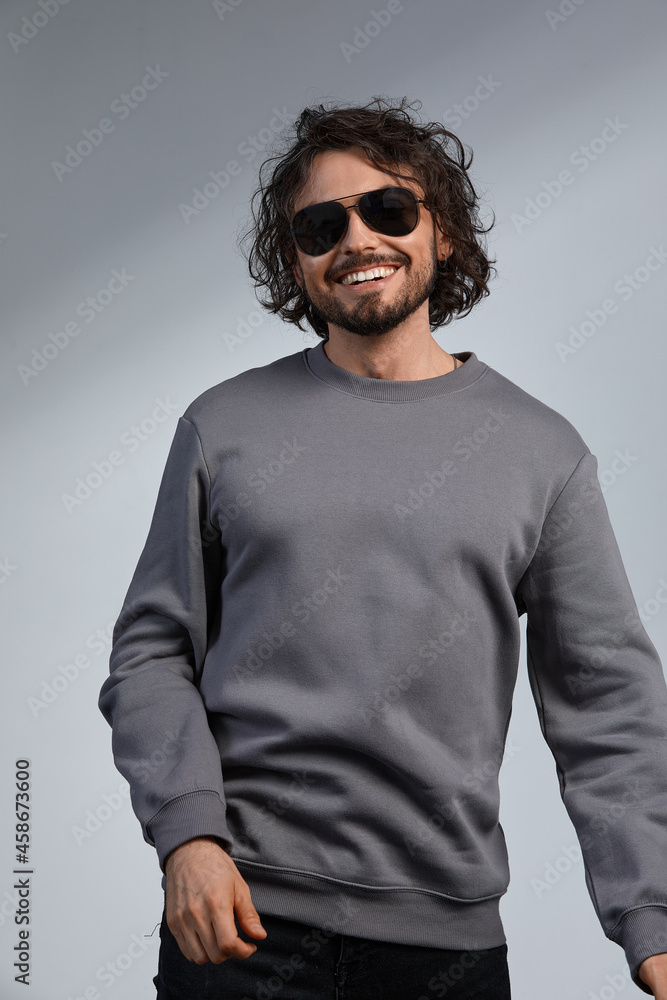indoor portrait of handsome freckled smiling male with curly hair, wears sepctacles posing for social advertisement, isolated on gray wall with copy space for your promotional information indoor portrait of handsome freckled smiling male with curly hair, wears sepctacles posing for social advertisement, isolated on gray wall with copy space for your promotional information