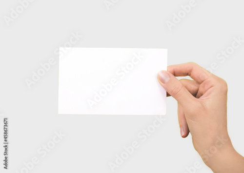 White card in a female hand on a light background. Business card in a woman's hand