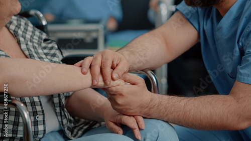Close up of hands of senior disabled woman and man nurse in nursing home. Medical assistant giving support and comforting retired person, caregiver helping with therapy and recovery