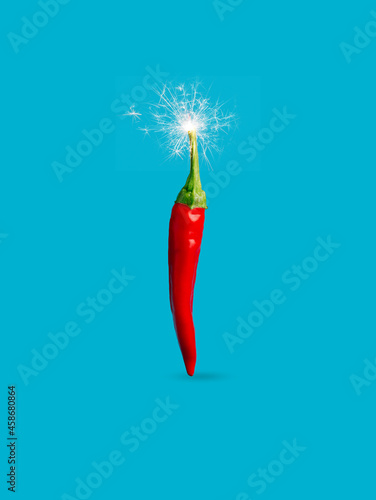 Obraz na płótnie Single red hot chili pepper with fire sparkler isolated on a vibrant blue background