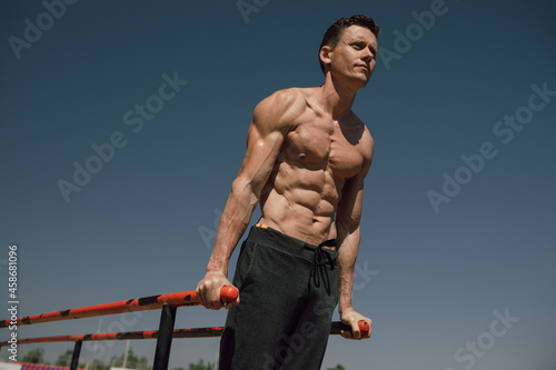  athlete man doing triceps dips on parallel bars in outdoor exercises. Calisthenic. Street workout photo