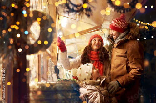 family, winter holidays and celebration concept - happy mother, father and little daughter at christmas market on town hall square in tallinn, estonia over lights