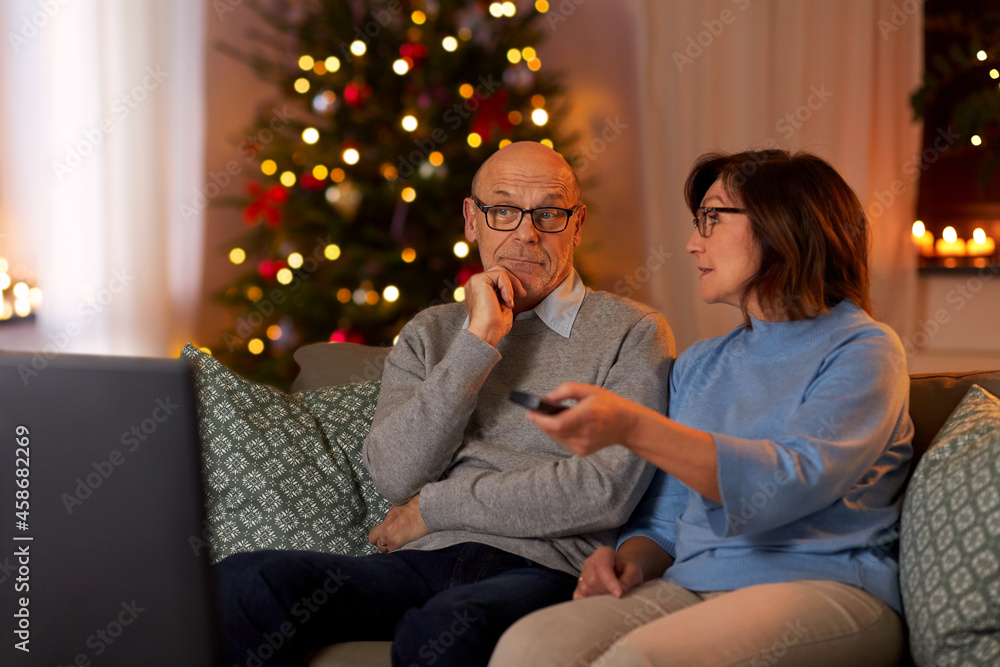 holidays, leisure and people concept - happy smiling senior couple watching tv at home in evening over christmas tree lights on background