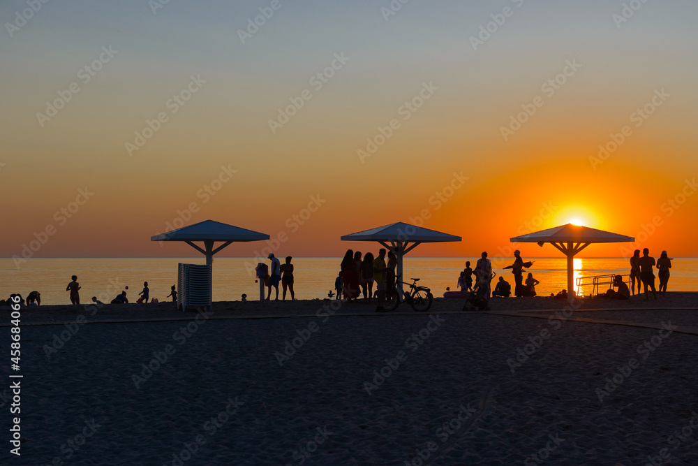 beach with umbrellas and silhouettes of people at sunset