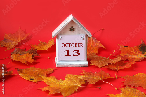Calendar for October 13 : decorative house with the name of the month in English, the number 13, autumn maple leaves on a red background, side view