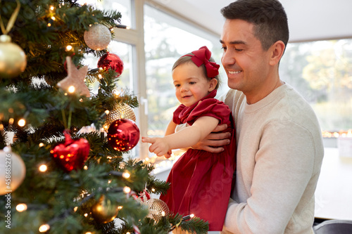 winter holidays and family concept - happy middle-aged father and baby daughter decorating christmas tree at home
