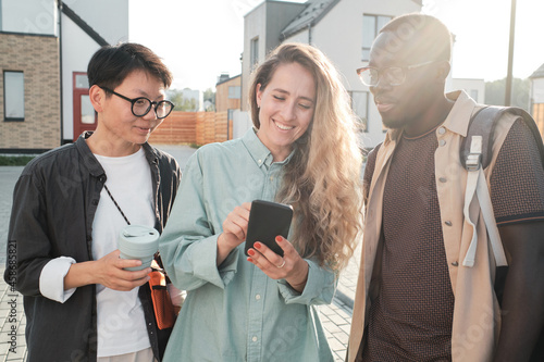 Horizontal medium portrait of three ethnically diverse friends hanging out together watching something in Internet on smartphone