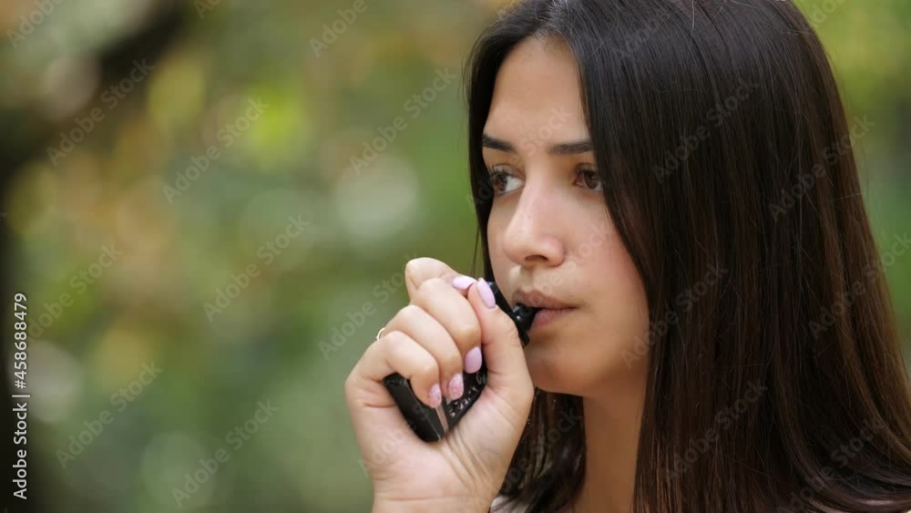 Stylish brunette girl standing and smoking e-cigarette in summer in slo-mo Stylish brunette girl standing and smoking e-cigarette in summer in slo-mo
