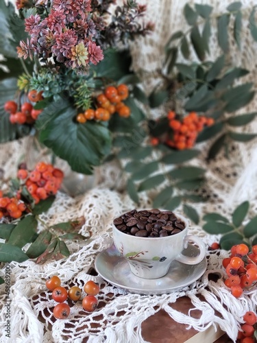Still life with cup and coffee beans, flowers and rowan on vintage tablecloth