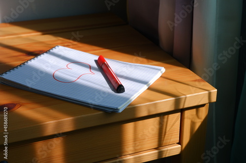 Drawing of a heart in a notebook. The sun's rays fall on the table and notebook. Valentine's Day.
